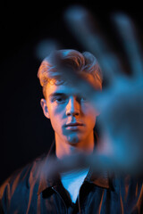 Introspective Young Man in Leather Jacket with Outstretched Hand and Dual-Colored Lighting