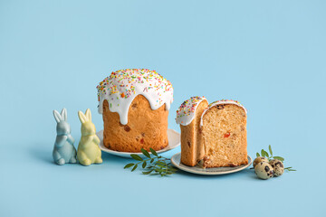 Plates with sweet Easter cakes, quail eggs and toy bunnies on blue background