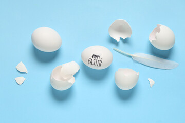 Egg with text HAPPY EASTER, shells and feather on color background