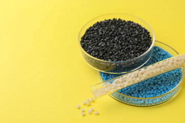 Colorful plastic granules in petri dishes and test tube on yellow background, closeup. Space for text