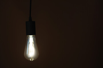 Glowing light bulb hanging on dark background. Space for text