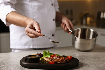 Professional chef adding sauce to delicious dish at table indoors, closeup