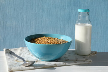Tasty oatmeal in bowl and milk served on white wooden table against light blue background, space for text