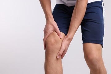 Young man suffering from pain in knee on light grey background, closeup