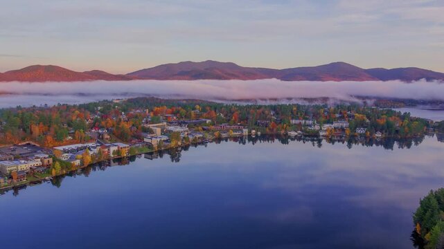 Stunning 4K drone footage of a minor lake in Lake Placid, Ithaca, NY, with autumn trees, houses, clouds, and mountains in the backdrop, captured at sunset.