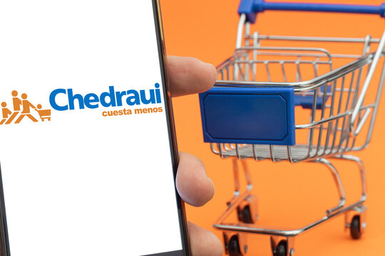 Mini grocery cart with blue handle and Chedraui logo in phone on orange background. Supermarket in Mexico. Supermarket concept.