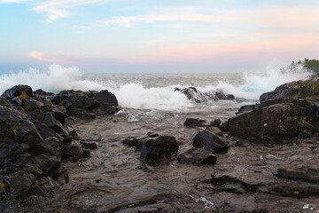 Waves crash along a rocky shoreline at sunrise.