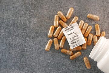 Gel capsules and silica gel packets scattered on a gray surface