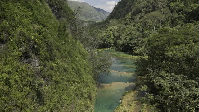 Drone flies northeast over limestone pools above the Cahabon River, deep in a green valley in Semuc Champey, Guatemala