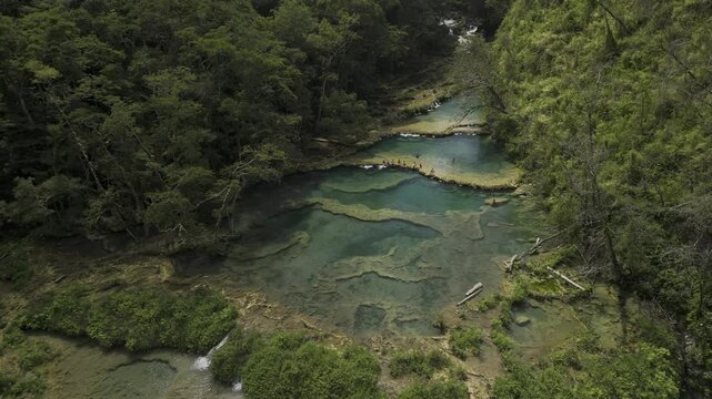 Drone flies low over most iconic spot of crystal clear limestone pools at the bottom of a green valley in Semuc Champey, Guatemala