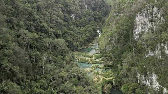 Drone flies through forested valley with steep walls above the Cahabon River and the limestone pools in Semuc Champey, Guatemala