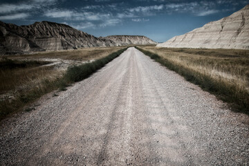 A desolate gravel road stretches towards the majestic mountains, inviting exploration while embodying a sense of adventure and freedom in vast nature.