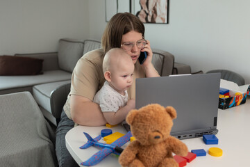 A parent skillfully multitasking with a small child while simultaneously using a phone and working on a laptop