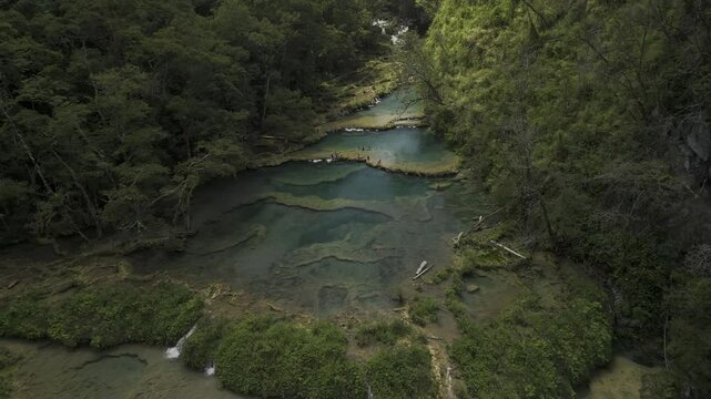 Drone flies up and away from the limestone pools over the Cahabon River in front of the K'anba Caves in Semuc Champey, Guatemala