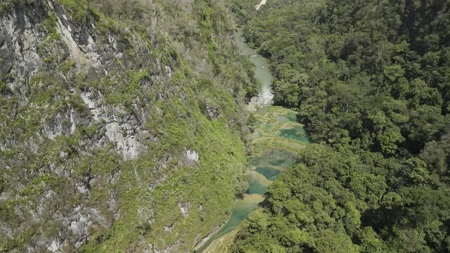 Drone orbits on southern bank of Cahabon River where the iconic crystal pools are lit up by the sunny  day in Semuc Champey, Guatemala