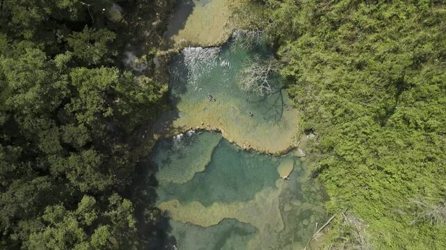 Drone flies backwards in bird's eye view with camera pointing straight down over crystal clear pools above the Cahabon River in Semuc Champey, Guatemala