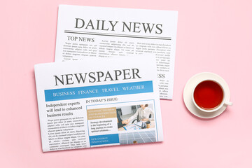 Newspapers with cup of tea on pink background