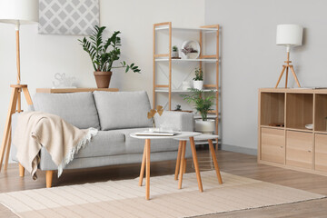 Interior of light living room with sofa, plaid, shelving unit and coffee table