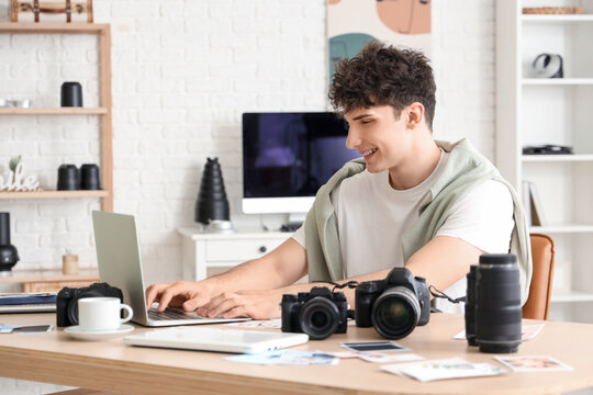 Professional happy male photographer with modern cameras and laptop working in studio