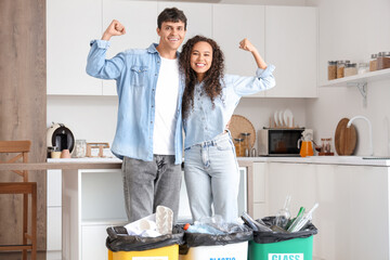 Happy young couple with garbage containers in kitchen. Waste sorting concept