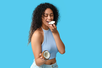 Beautiful young African-American woman with halves of fresh coconut on blue background