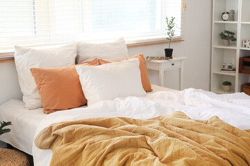 Big comfortable bed with crumpled linen, bedside table and houseplants in bedroom