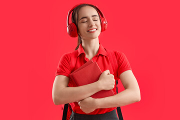 Female student in headphones with books on red background