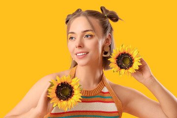 Beautiful young happy woman with stylish makeup and sunflowers on yellow background