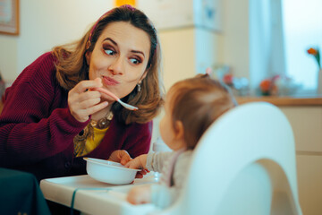 Funny Mom Spoon Feeding her Infant in a High Chair. Mother using silly faces and airplane method at the mealtime 
