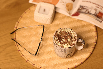 Cup of hot chocolate with whipped cream, eyeglasses and book on tray in room, top view