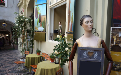 A charming European cafe scene with outdoor seating, featuring white roses, artistic details like...