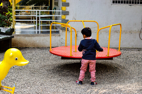 Young child playing alone in a park with merry go round