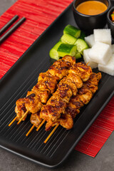 Grilled chicken satay skewers with peanut sauce, rice cakes, and vegetables