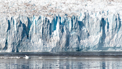 The image captures the stunning majesty of a towering glacier, with its blue and white hues reflecting in the calm waters below, illustrating the beauty of nature’s frozen wonders.