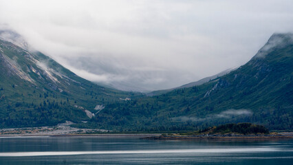 Obraz premium A breathtaking view of misty mountains enveloped in clouds, reflecting over still waters, portraying the serenity and beauty of untouched nature.