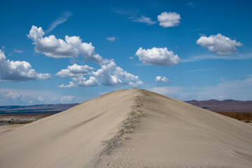 A captivating view of an endless sand dune under a bright blue sky dotted with fluffy clouds, evoking feelings of adventure and exploration in a desert landscape.