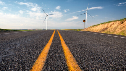 A scenic view of an open road lined with wind turbines, symbolizing renewable energy and sustainability in a beautiful, expansive landscape.