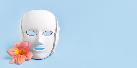 Cosmetic LED facial mask regenerative treatment on blue background with flowers lilies. Health and beauty of the face. Taking care of yourself and your face, anti-aging, prolonging youth and beauty
