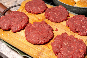 Fresh, raw hamburger patties on a wooden cutting board, ready for cooking. The texture and arrangement highlight the simplicity of burger preparation.