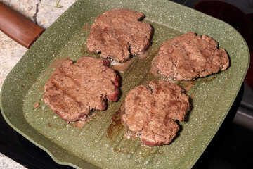 Four sizzling hamburger patties cook on a green griddle, showing texture, grease, and browning. A snapshot of burger preparation at its finest.