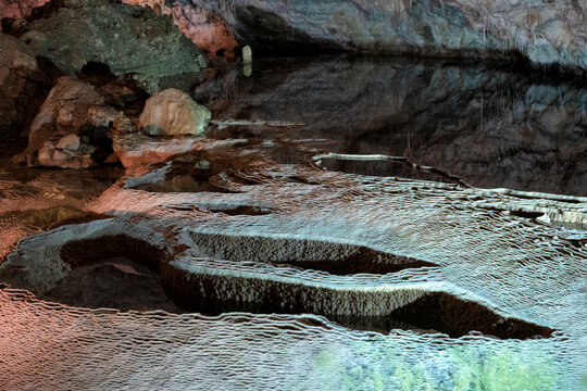 The image captures an intriguing underground cave with stunning stalactite formations reflected in still water, showcasing nature's artistry in a serene environment.