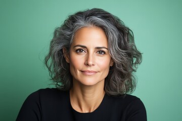 Fototapeta premium Mature woman with voluminous gray curls looking serene against a minimalist green background symbolizing wisdom self confidence and aging gracefully in high definition portrait