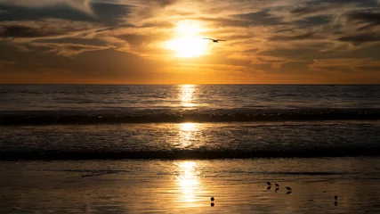 Fototapeten Wohnzimmer The peaceful image of a sunset cast over calm waters, showcasing soft golden hues contrasted against the light clouds, represents serenity and the beauty of nature.  © Valerii