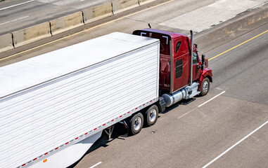 Burgundy high cab bonnet big rig semi truck transporting cargo in refrigerator semi trailer with...
