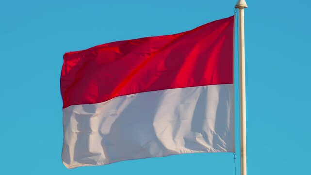 The flag of Monaco waving with the blue sky on the background