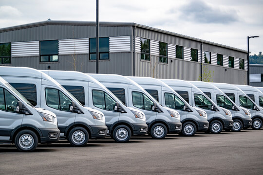 Compact gray cargo commercial mini vans standing in row on industrial warehouse parking lot waiting for the next local deliveries