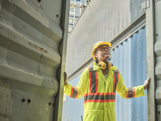 Photo of a logistics worker or male engineer in safety gear at a container yard inspecting a container that is about to be shipped to the port.