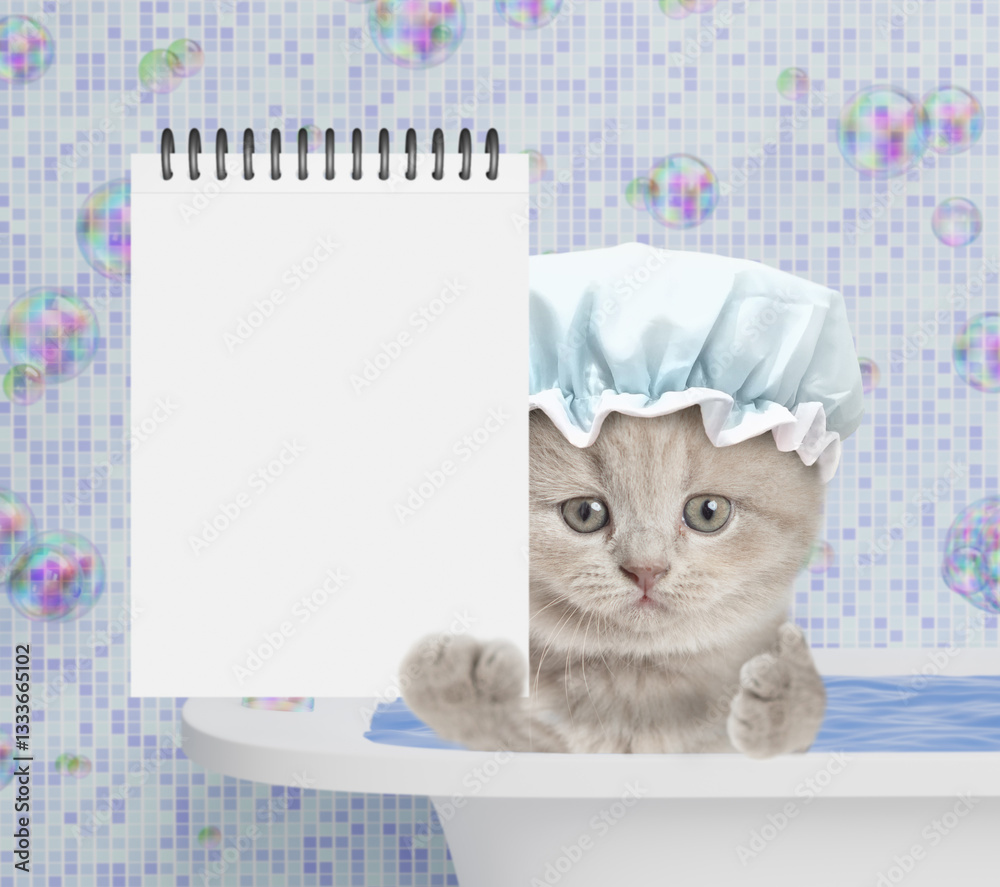 Aufkleber cute kitten wearing shower cap takes the bath at home and shows blank white notepad in it paw. empty