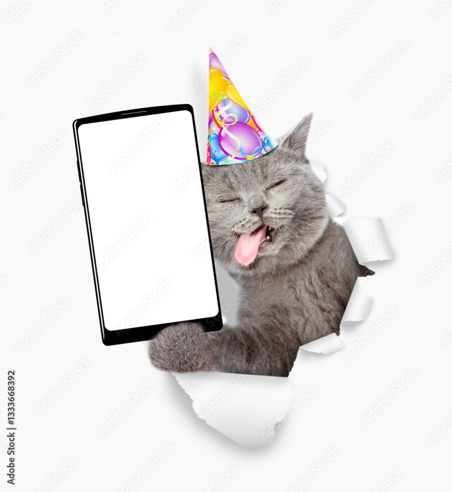 Poster Happy cat with tongue out wearing party cap showing smartphone with white blank screen in it paw through torn white paper hole. Empty free space for mock up, banner