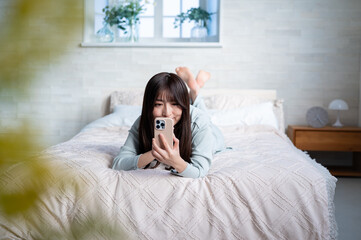 Obraz premium うつ伏せでスマホを操作する日本人女性